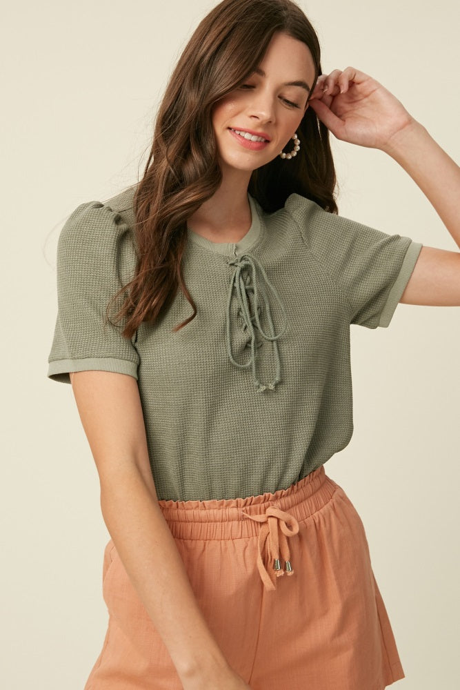woman wearing a green short sleeve top with lace-up front and peach drawstring shorts