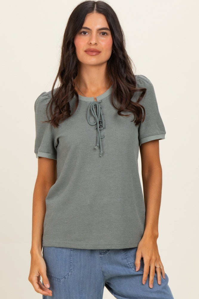 woman wearing a sage green short sleeve top with a tie-front detail and puff sleeves