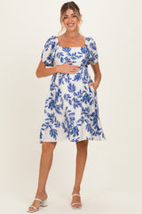 woman wearing a blue and white floral print maternity dress with puff sleeves and pockets, holding her baby bump