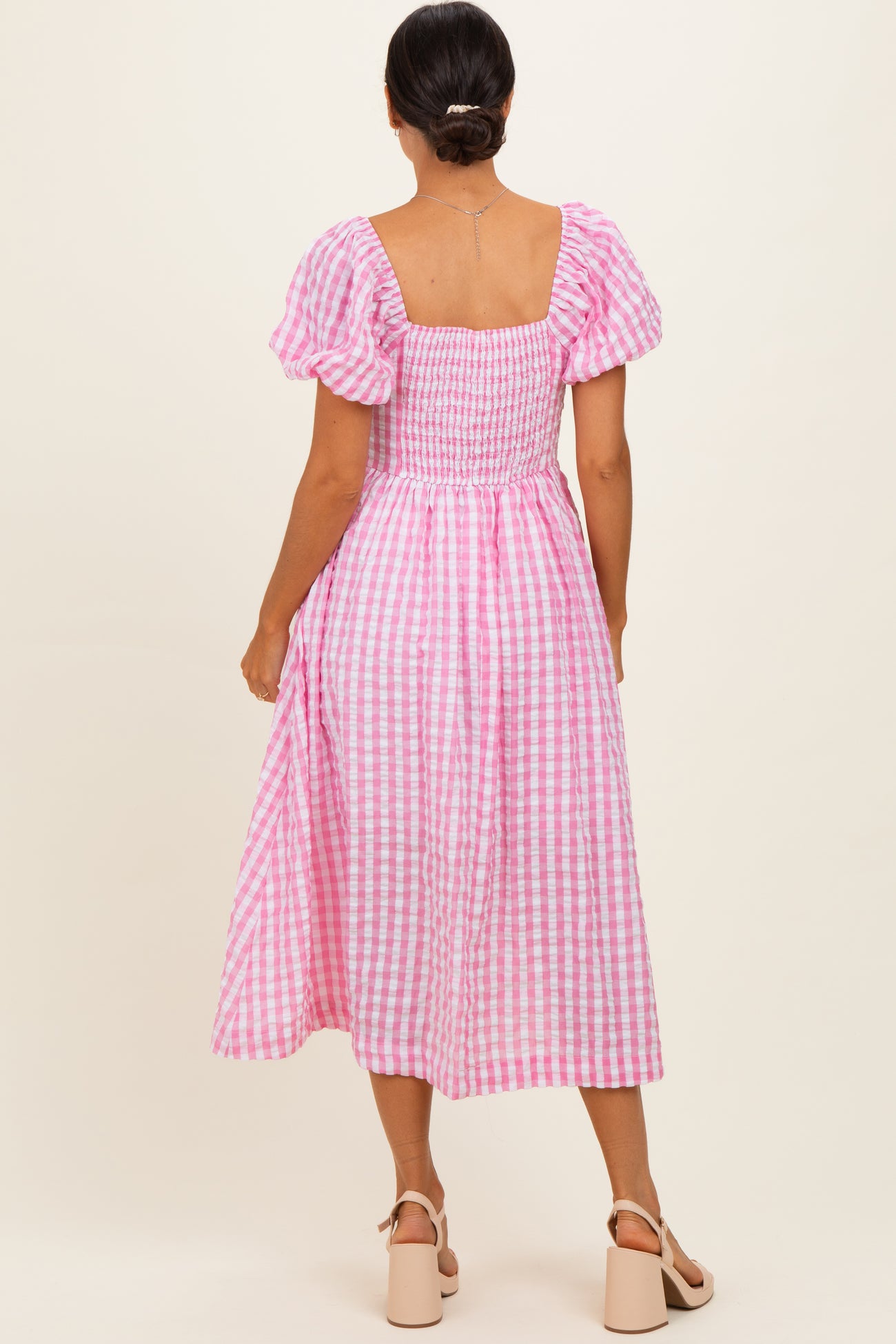 woman wearing a pink and white gingham midi dress with puff sleeves and a smocked bodice, seen from the back
