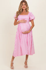 woman wearing a pink and white gingham maternity dress with puff sleeves and holding her baby bump