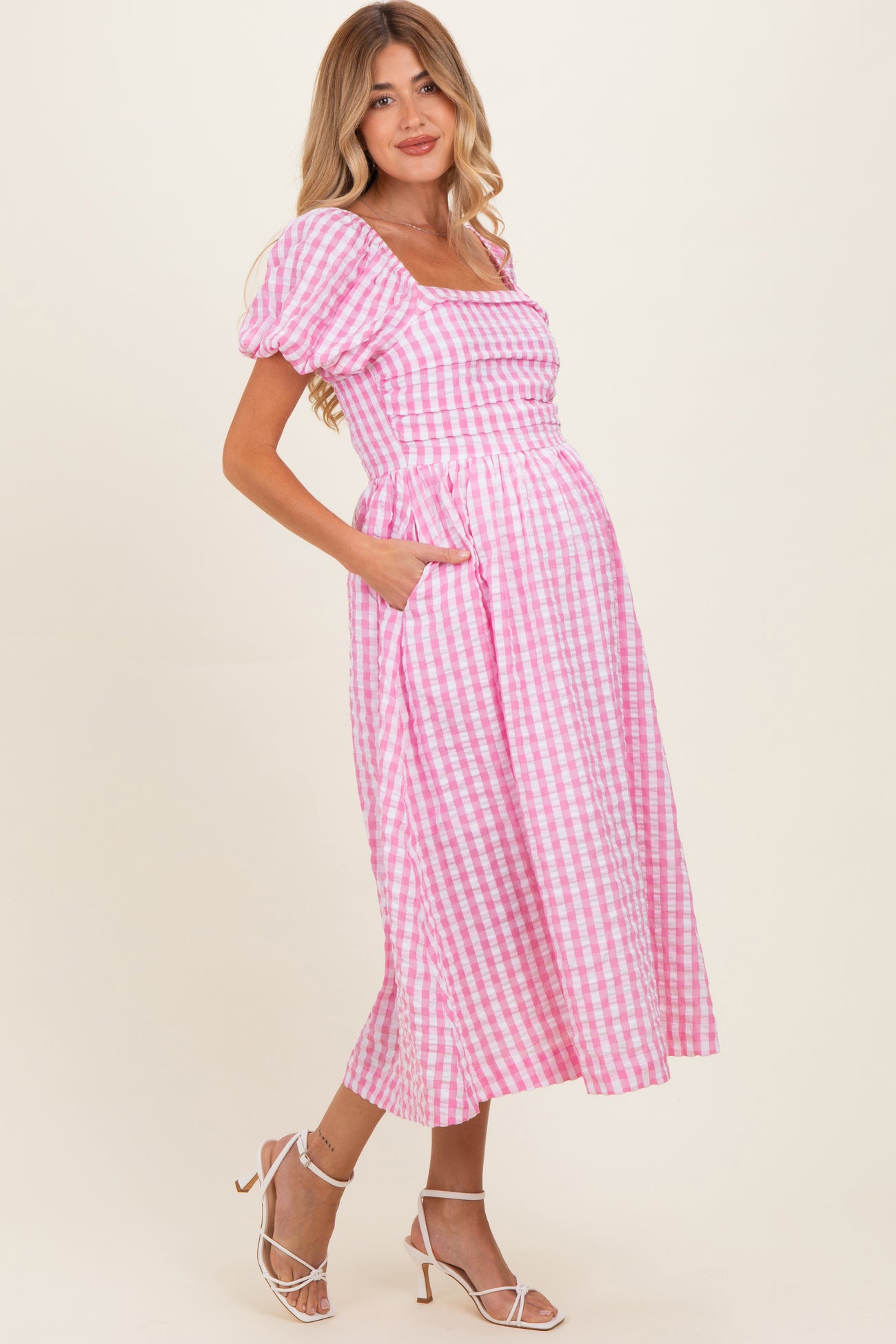 woman wearing a pink and white gingham maternity dress with puff sleeves and pockets, showcasing her baby bump
