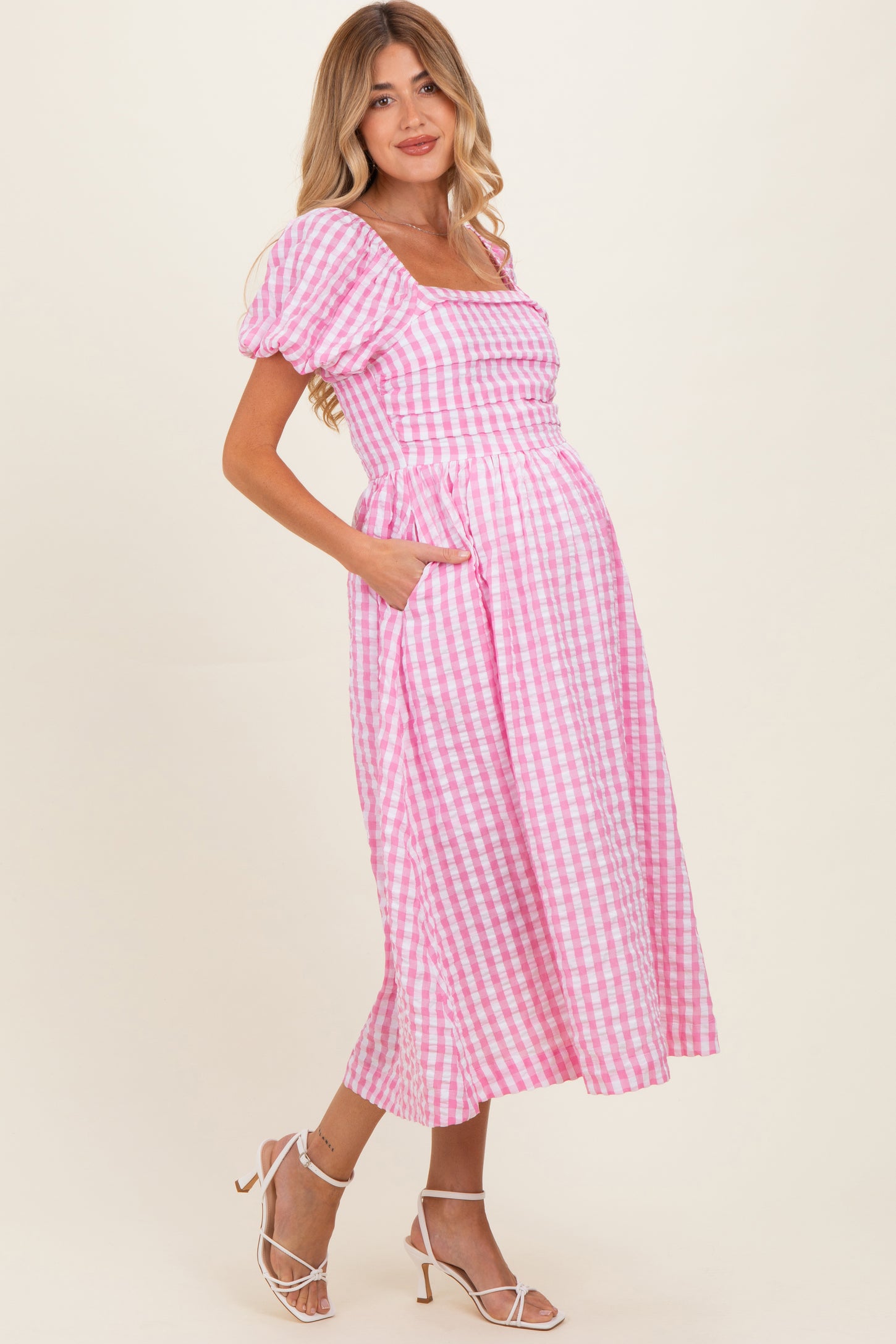 woman wearing a pink and white gingham maternity dress with puff sleeves and pockets, showcasing her baby bump