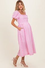 woman wearing a pink and white gingham maternity dress with puff sleeves and pockets, showcasing her baby bump