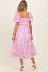 woman wearing a pink and white gingham maternity dress with puff sleeves and a smocked bodice, showing a baby bump from behind