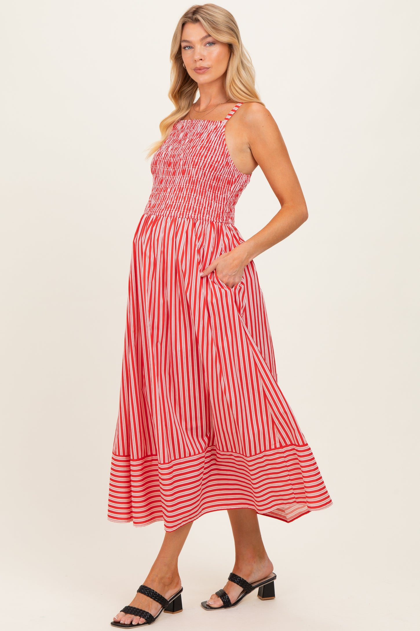 woman wearing a red and white striped maternity dress with a smocked bodice and pockets, showcasing her baby bump