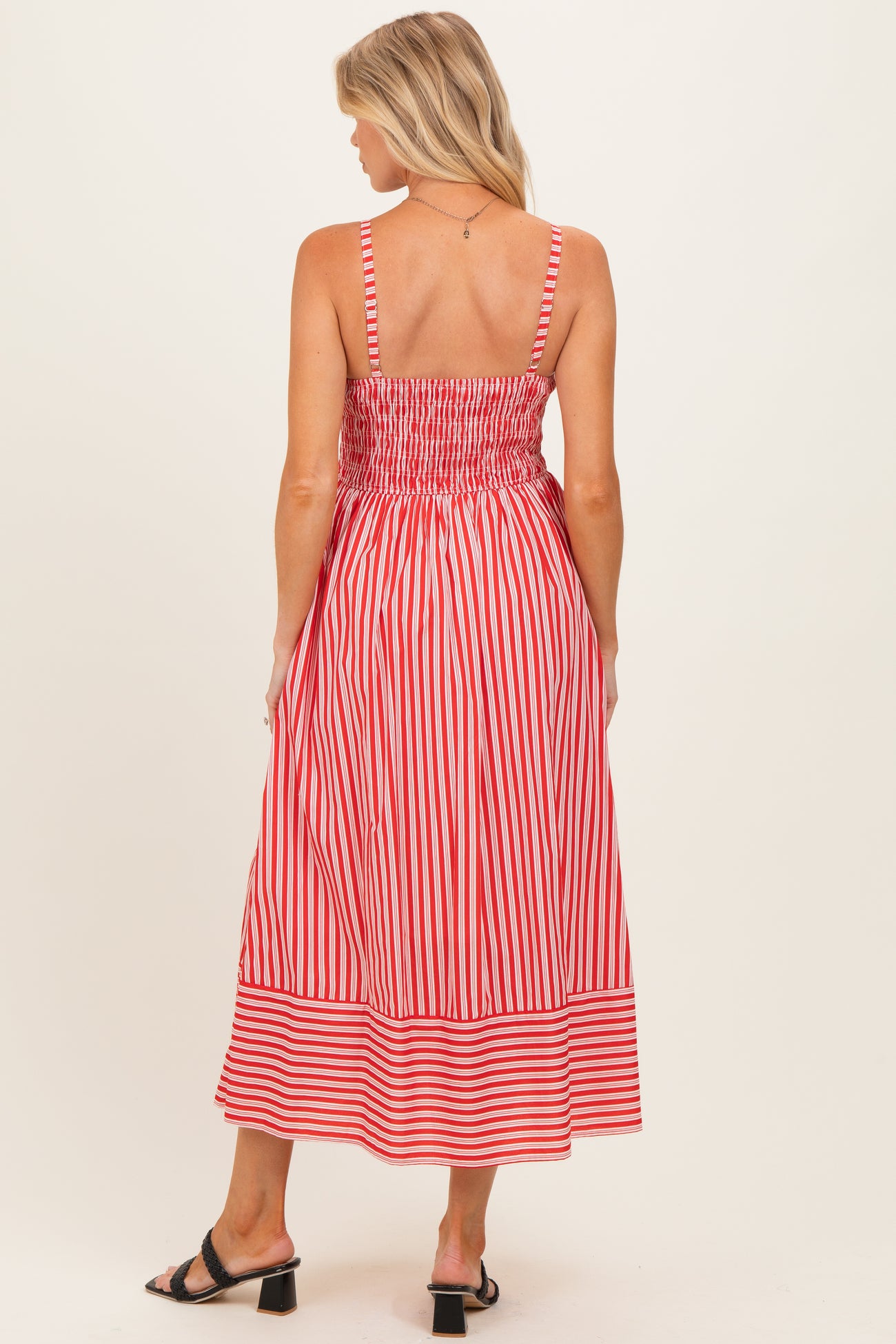 woman wearing a red and white striped maternity dress with a smocked back and midi length in a casual style