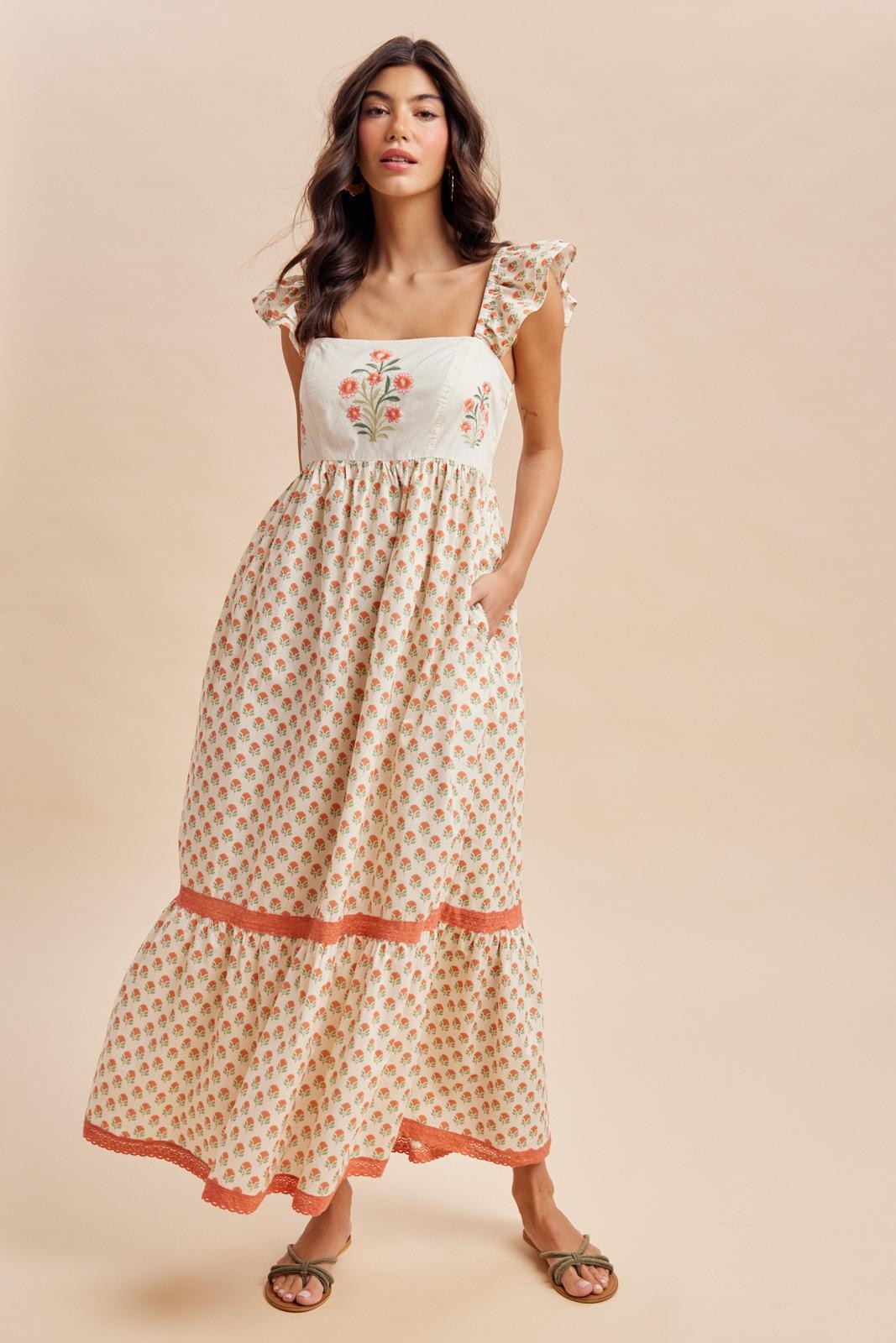 woman wearing a white floral embroidered maxi dress with ruffled sleeves and a tiered hemline