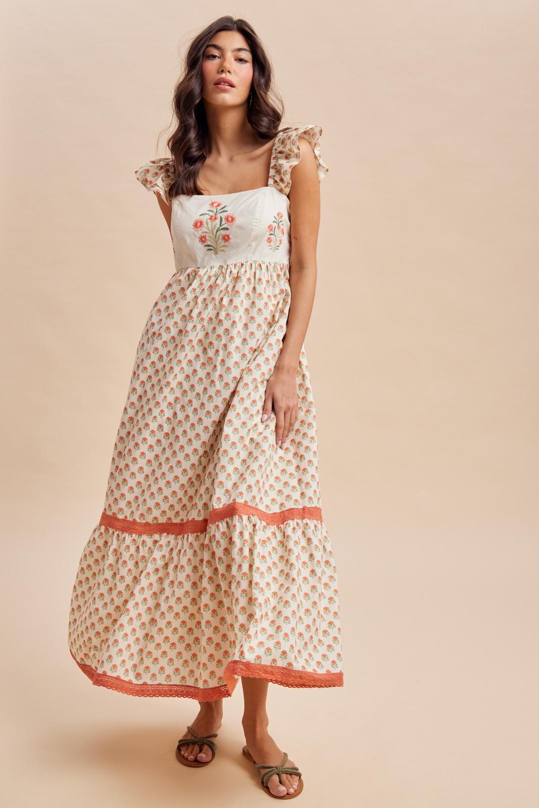 woman wearing a cream floral maxi dress with ruffled sleeves and orange trim
