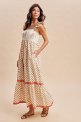 woman wearing a cream maxi dress with floral embroidery, ruffle straps, and pockets, styled with flat sandals