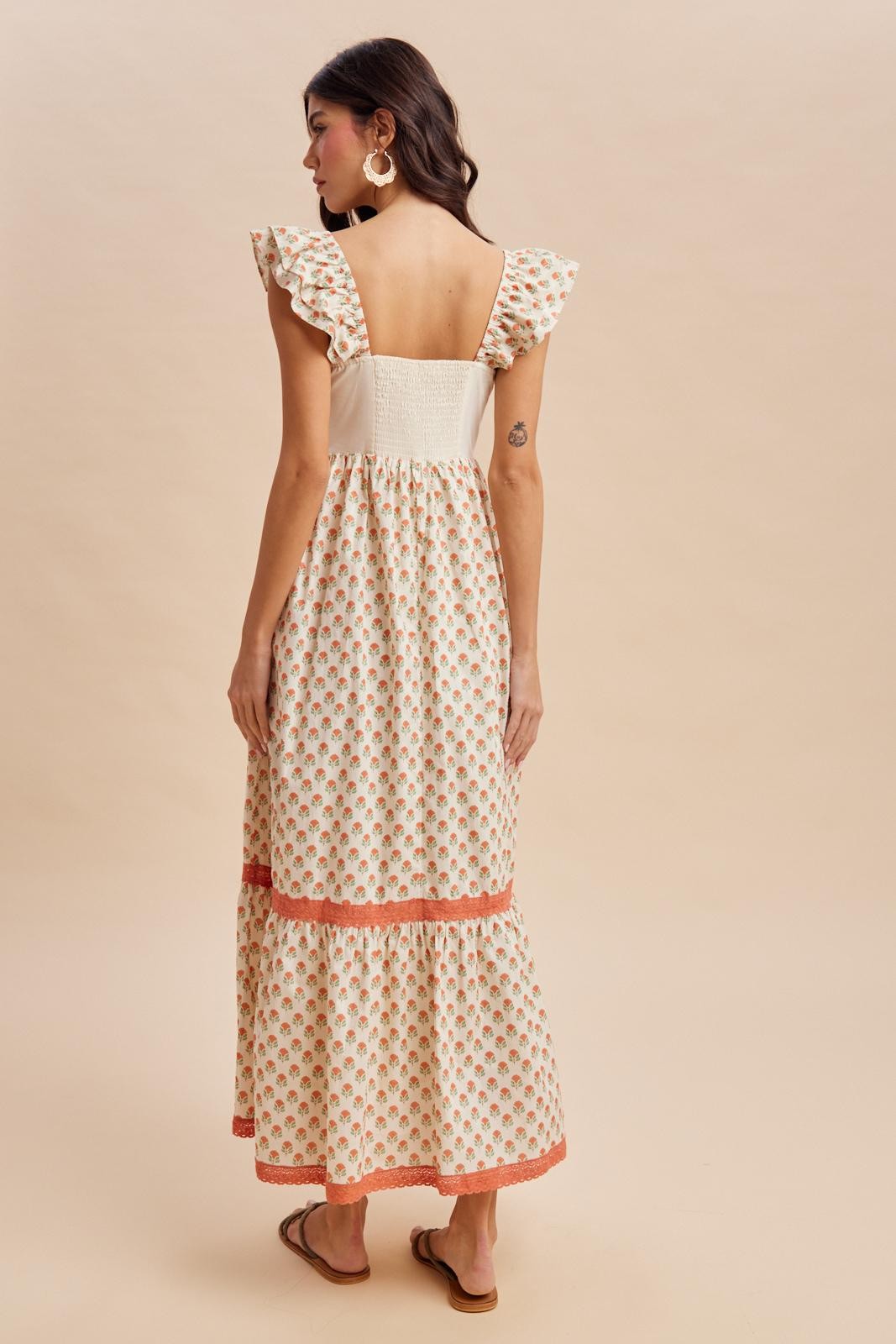 woman wearing a cream floral maxi dress with ruffled sleeves and a tiered hem, showing the back view