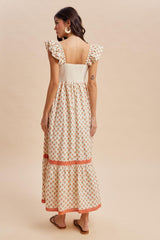 woman wearing a cream floral maxi dress with ruffled sleeves and a tiered hem, showing the back view