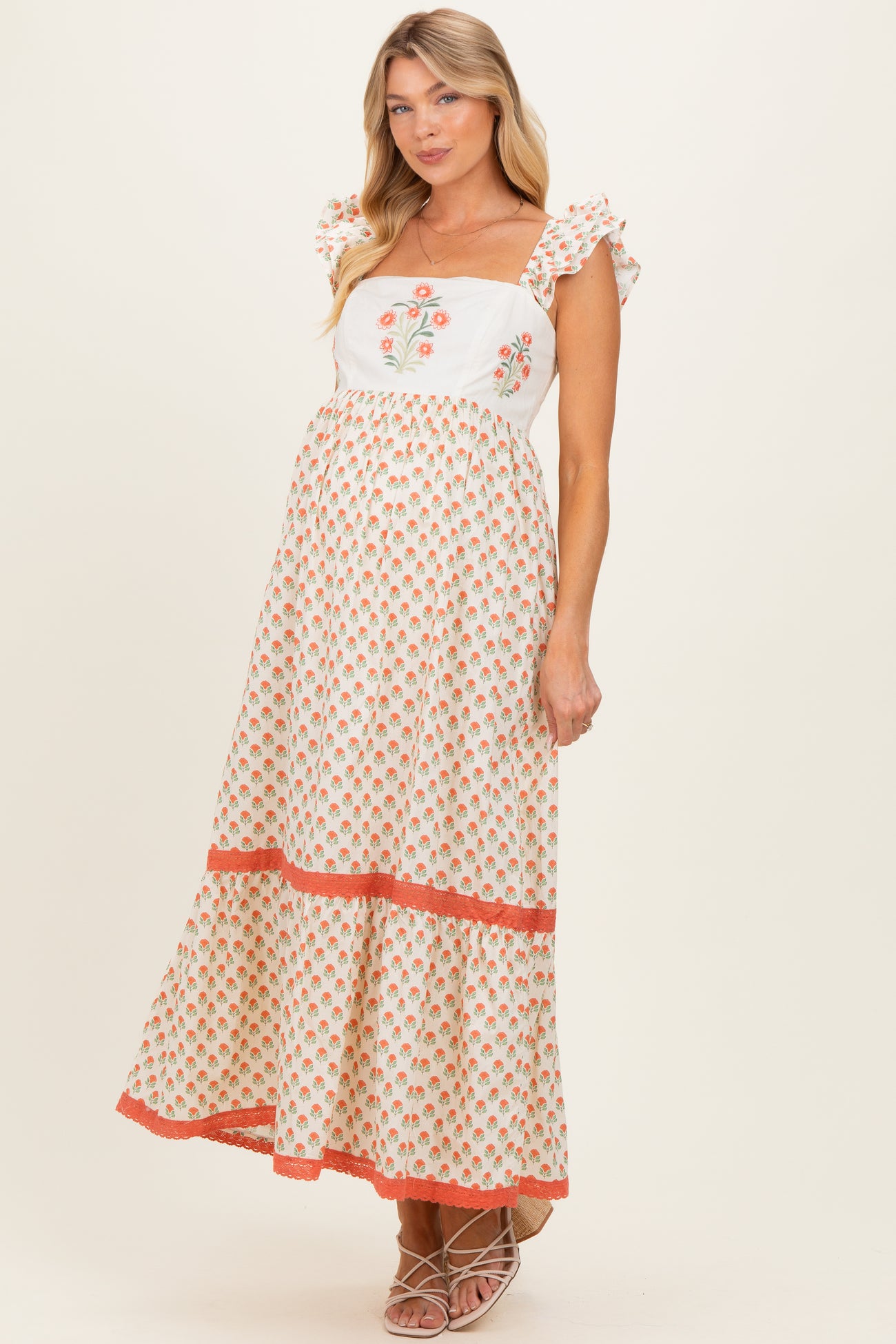 woman wearing a floral print white and peach maternity maxi dress with ruffle sleeves and a baby bump visible