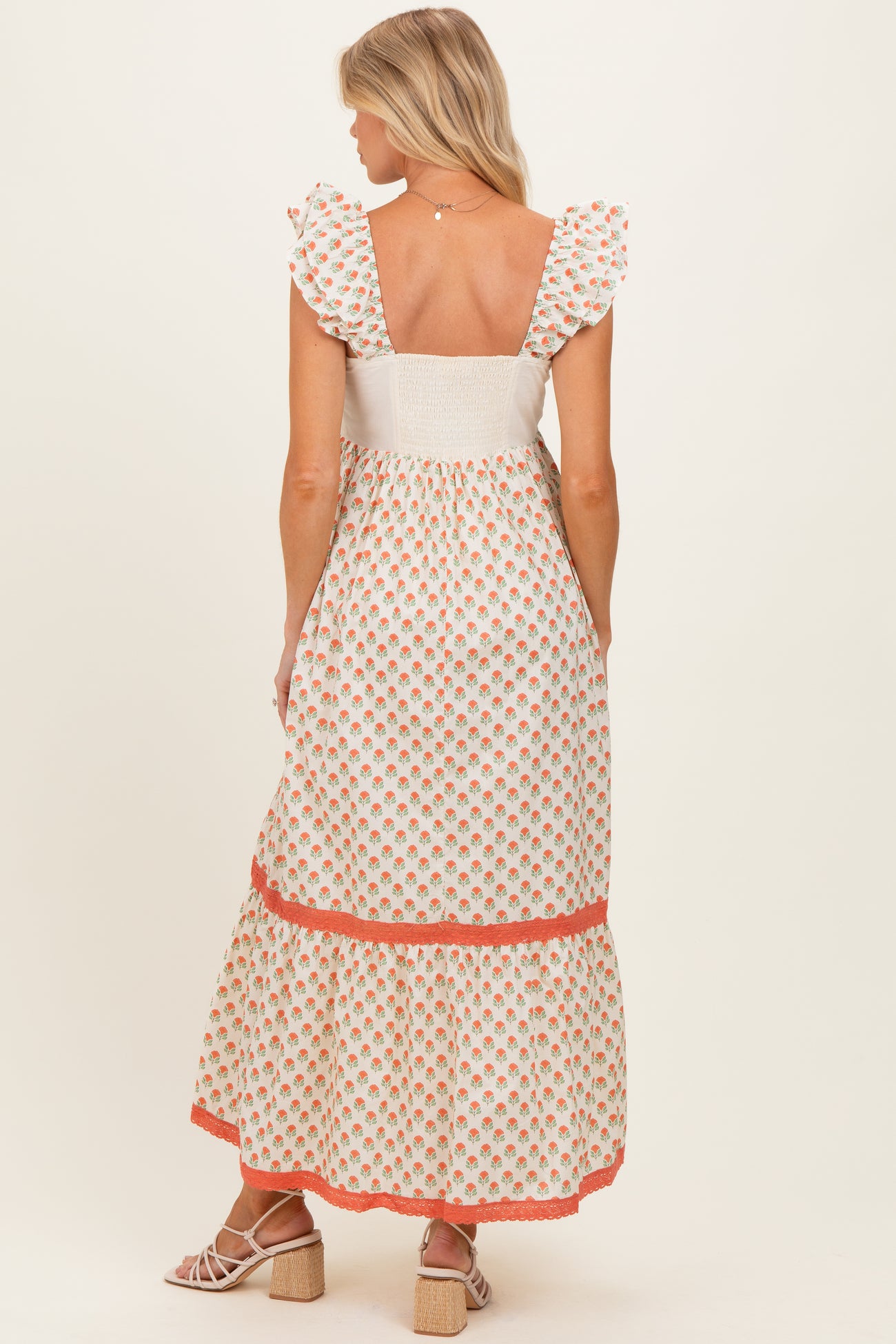 woman wearing a white floral maternity maxi dress with ruffled sleeves and a tiered hem, showing her pregnant belly from the back