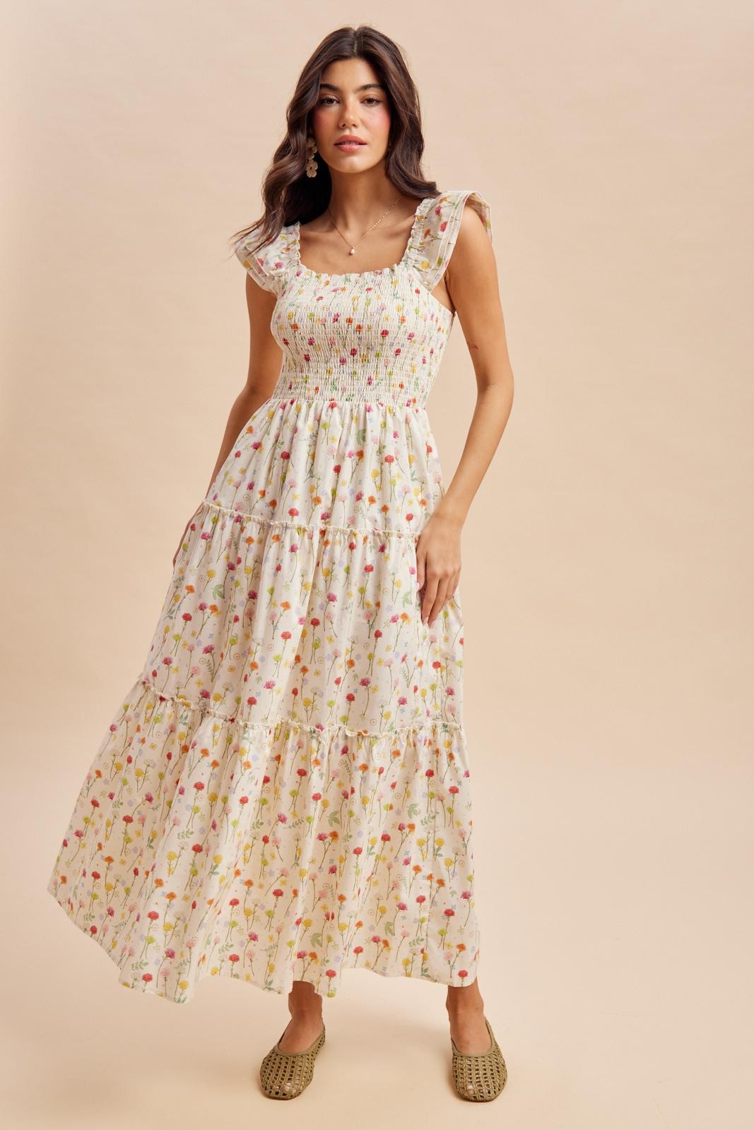 woman wearing a floral maxi dress with smocked bodice and tiered skirt, standing against a neutral background