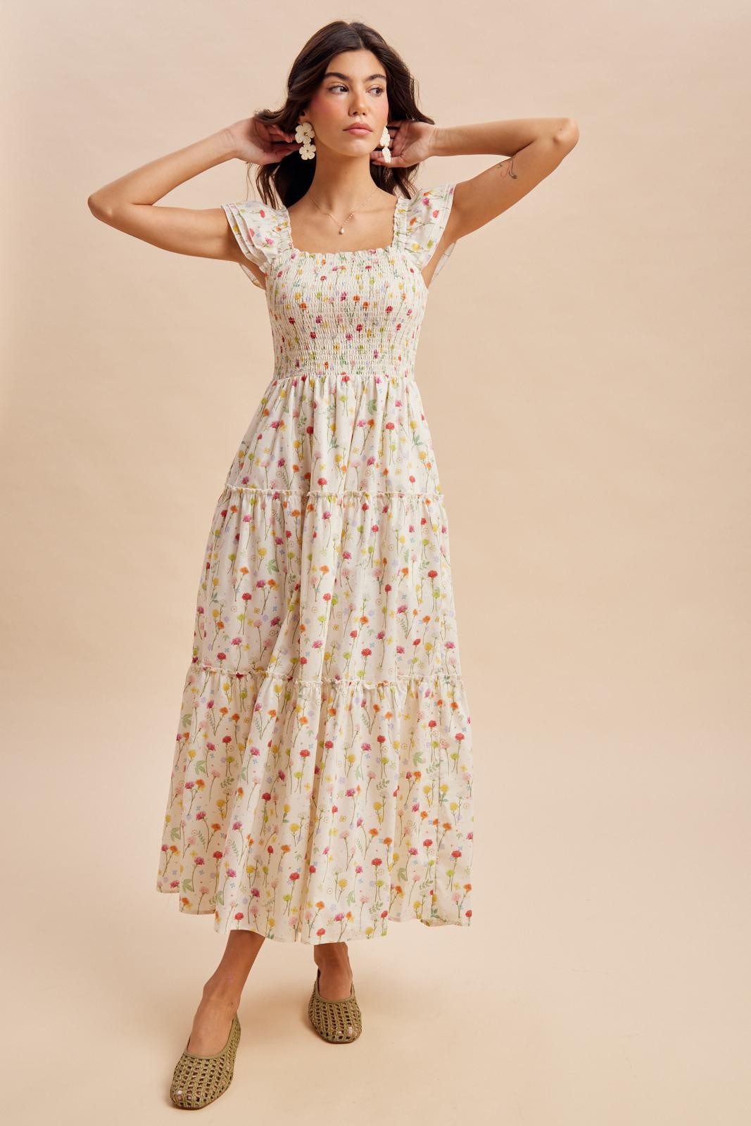 woman wearing a floral printed maxi dress with a square neckline and tiered skirt, styled with green slip-on shoes