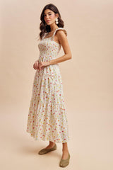 woman wearing a floral print maxi dress with smocked bodice and tiered skirt, paired with green woven shoes