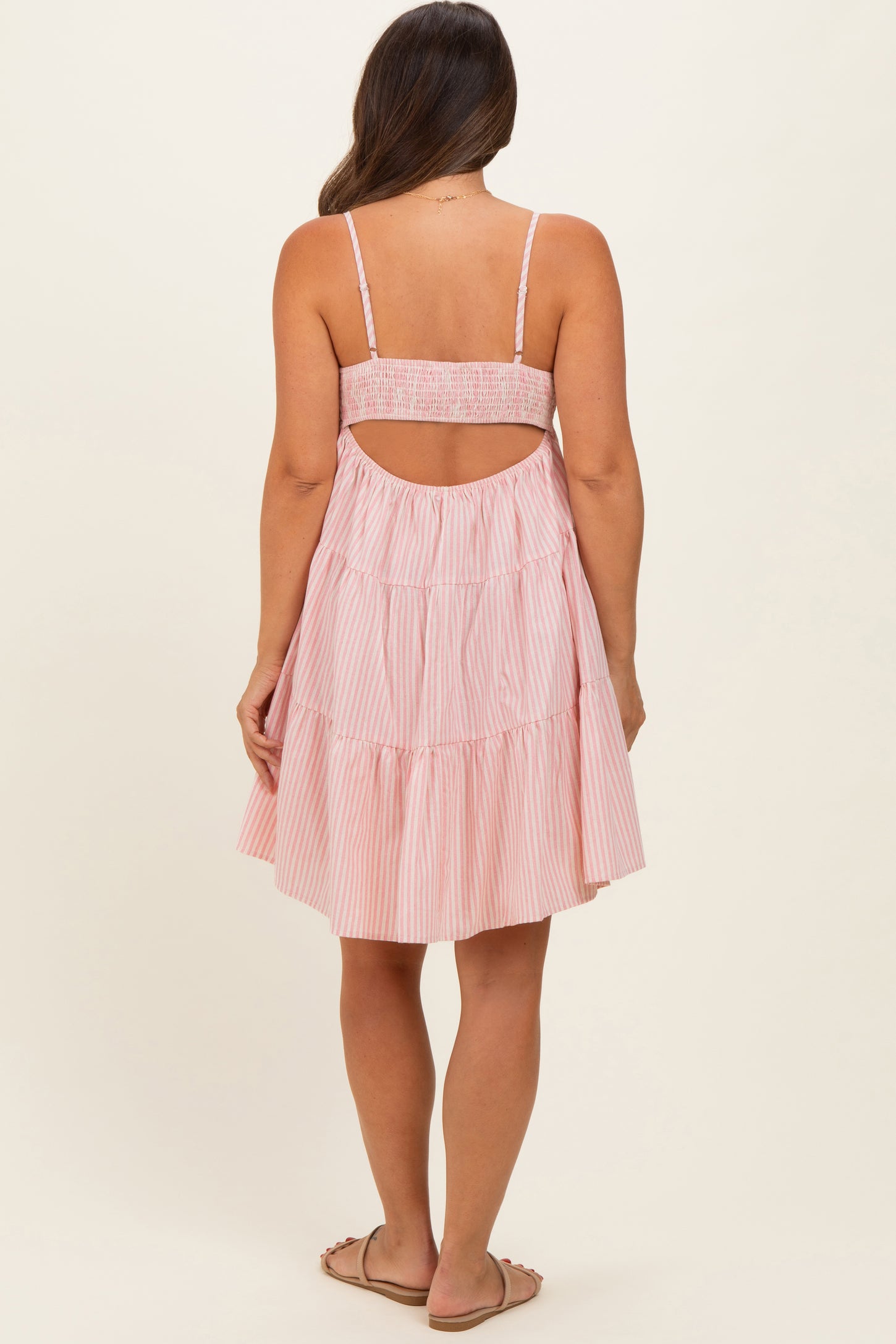 woman wearing a pink and white striped maternity dress with a tiered skirt and open back design