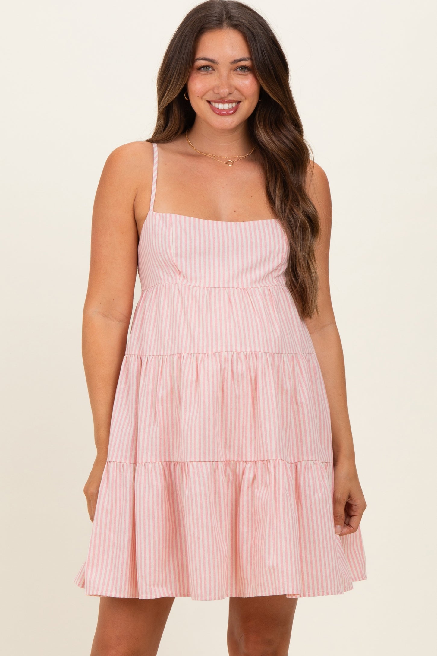 woman wearing a pink and white striped maternity dress with a tiered skirt and thin straps, showcasing her baby bump