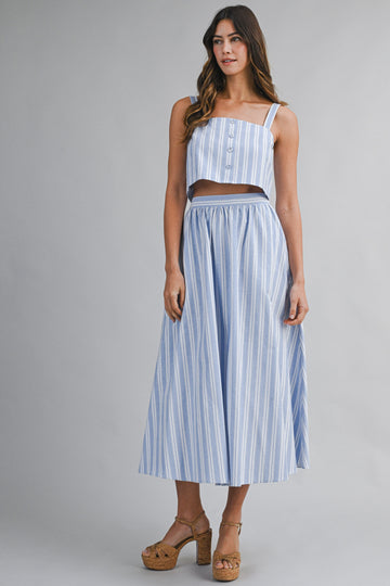 woman wearing a blue and white striped two-piece dress with a cropped top and long skirt, standing on platform heels