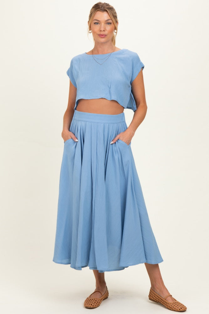woman wearing a light blue cropped top and matching maxi skirt, showcasing a baby bump and styled with flat shoes
