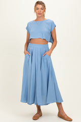 woman wearing a light blue cropped top and matching maxi skirt, showcasing a baby bump and styled with flat shoes