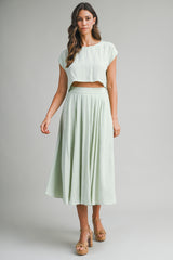 woman wearing a light green cropped top and matching pleated maxi skirt with a flowy silhouette and platform sandals