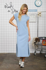 woman wearing a light blue maxi dress with short sleeves and side slits, standing in a laundry-themed setting