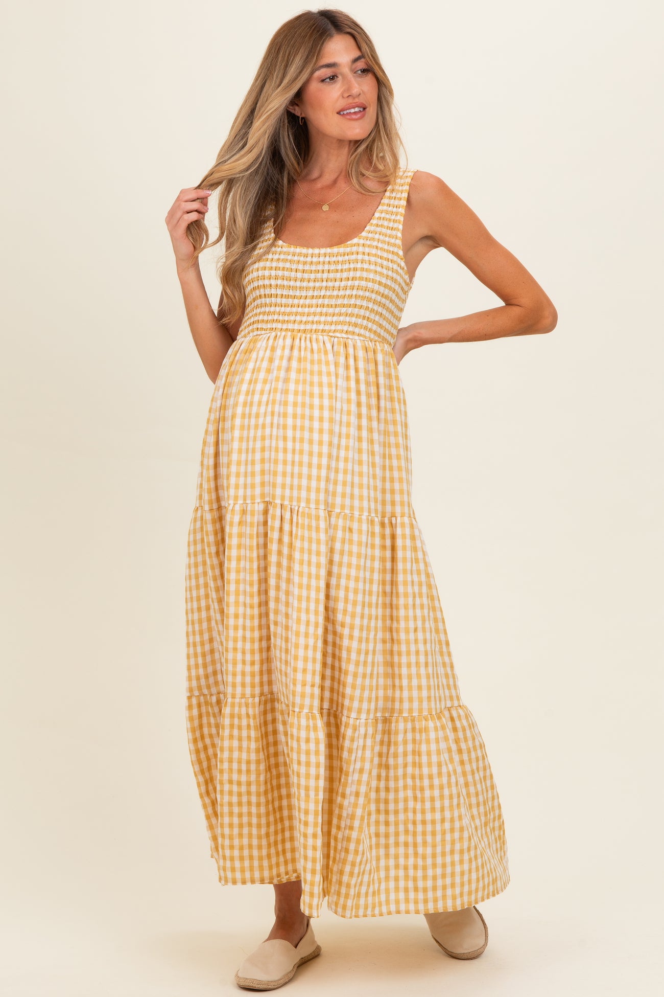 woman wearing a yellow gingham maternity maxi dress with smocked bodice and tiered skirt, showing her baby bump