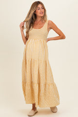 woman wearing a yellow gingham maternity maxi dress with smocked bodice and tiered skirt, showing her baby bump