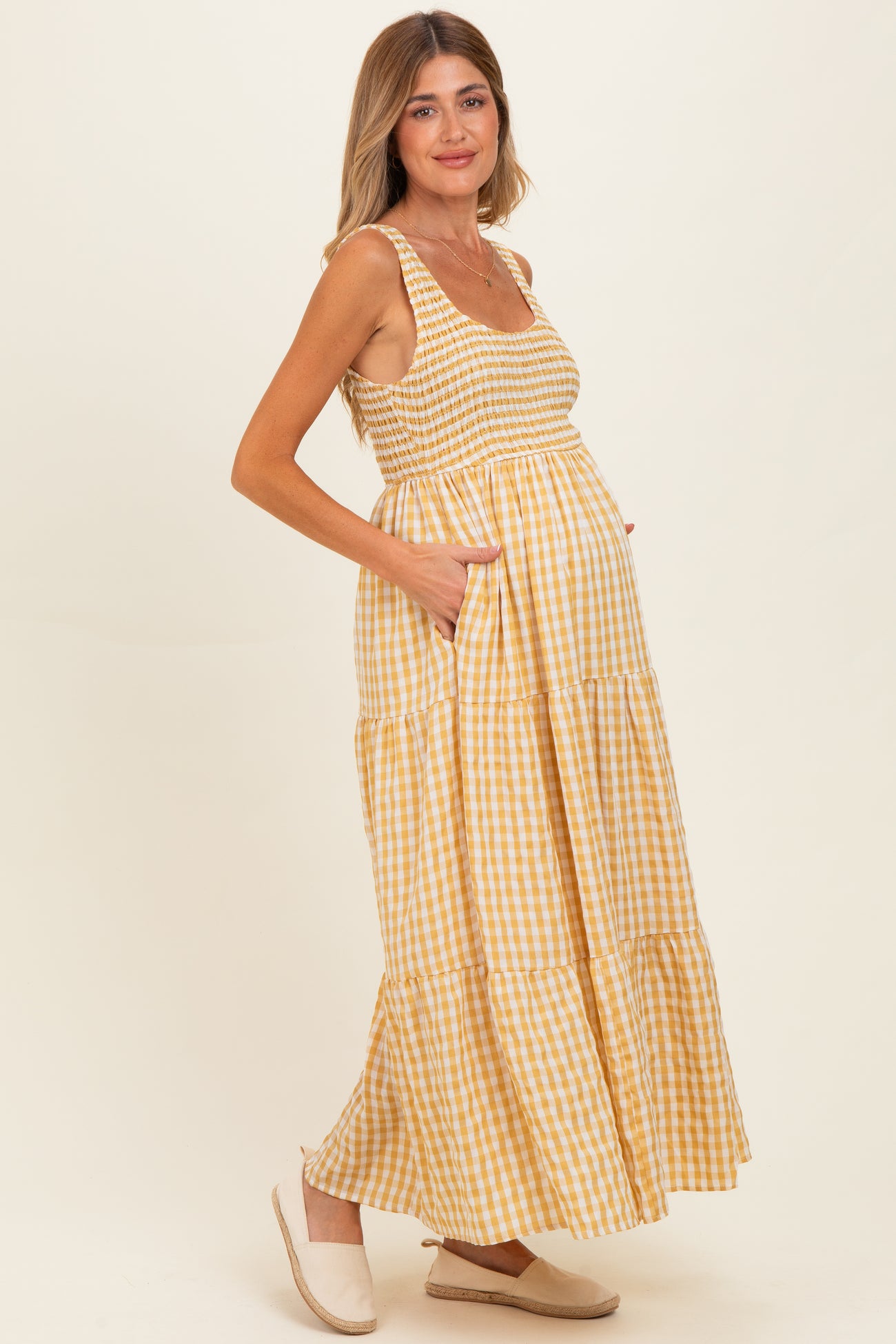 woman wearing a yellow and white gingham maternity maxi dress with pockets and a visible baby bump