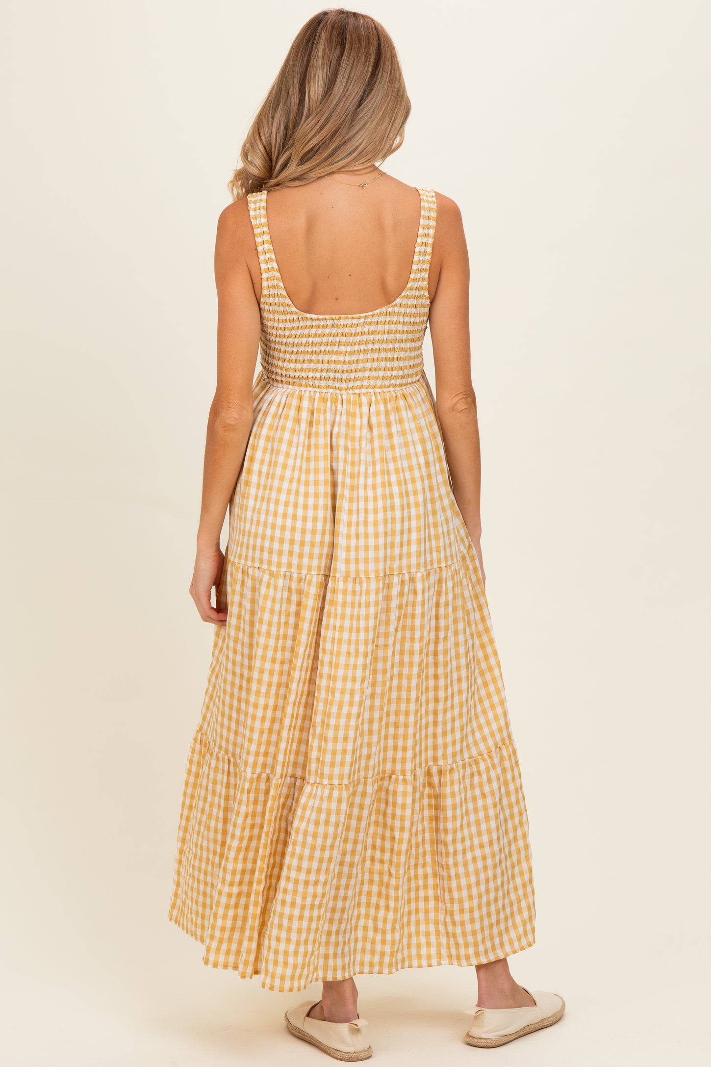 woman wearing a yellow gingham maternity maxi dress with a smocked bodice and tiered skirt, showing her back