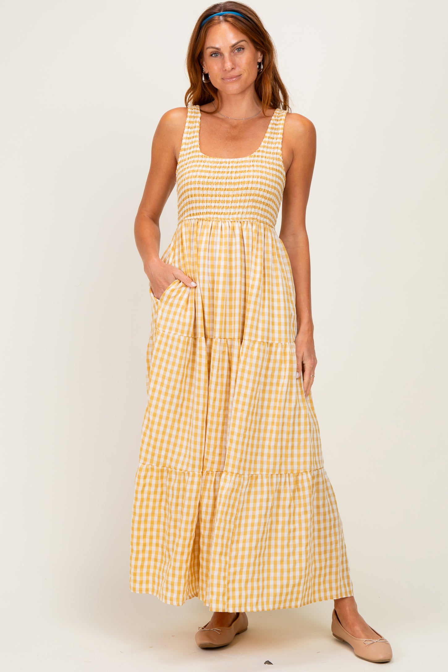 woman wearing a yellow and white gingham sleeveless maxi dress with smocked detailing and side pockets
