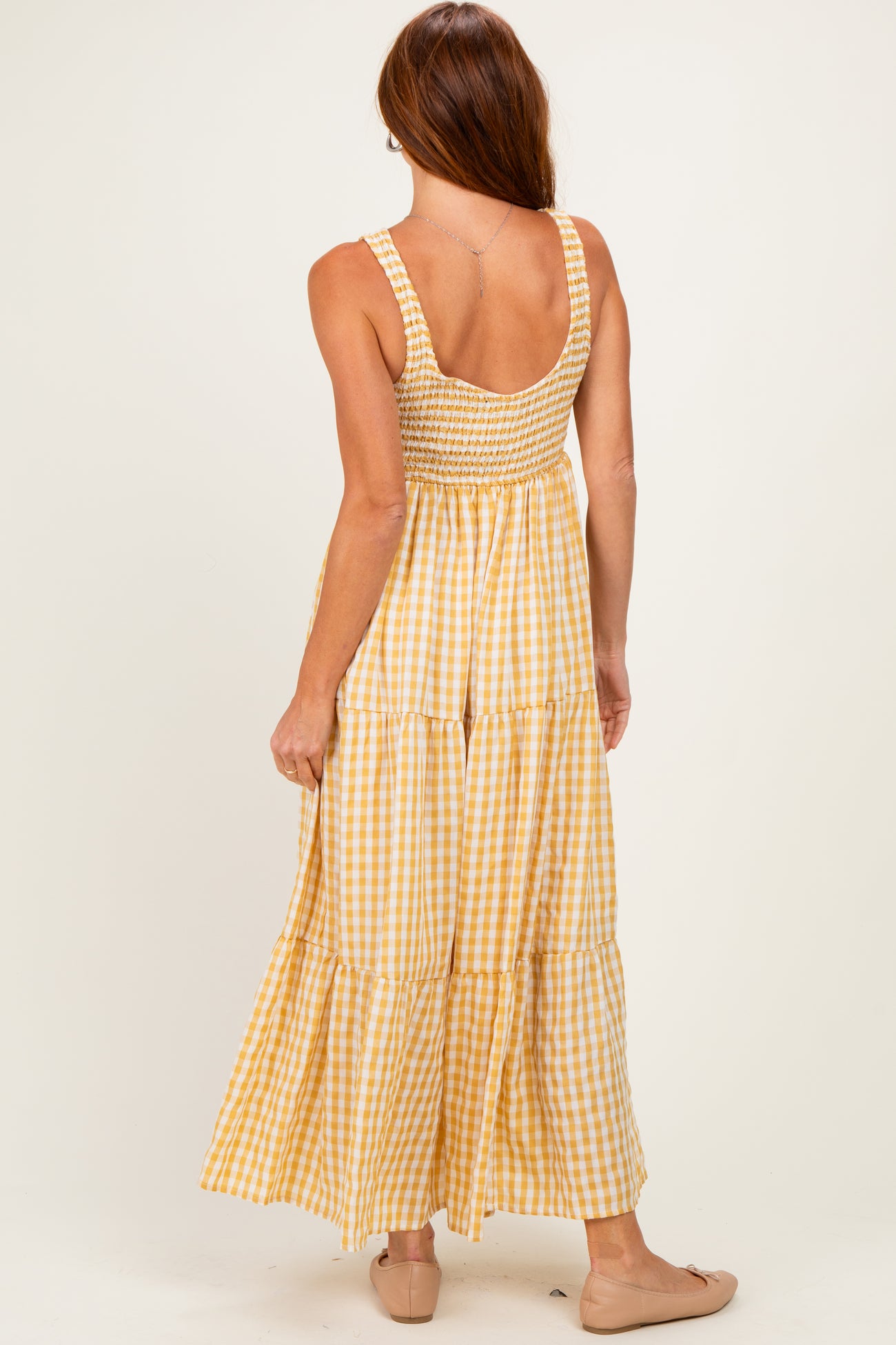 woman wearing a back view of a yellow and white gingham maxi dress with smocked bodice and tiered skirt