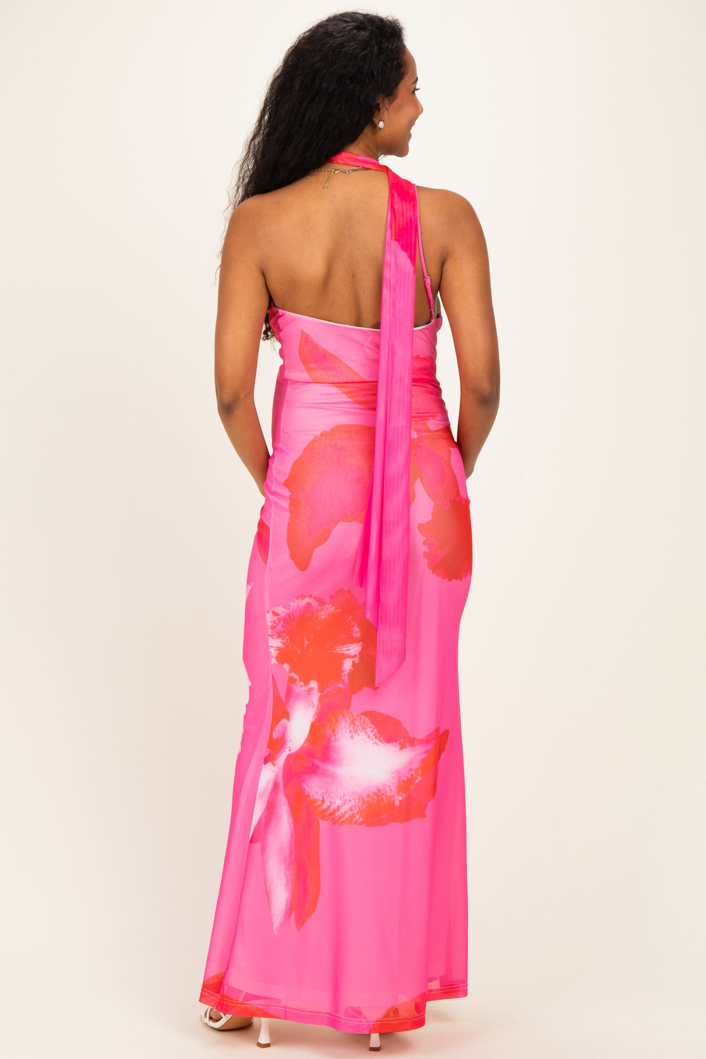 woman wearing a vibrant pink maternity dress with large floral patterns and a halter neck, showing her back