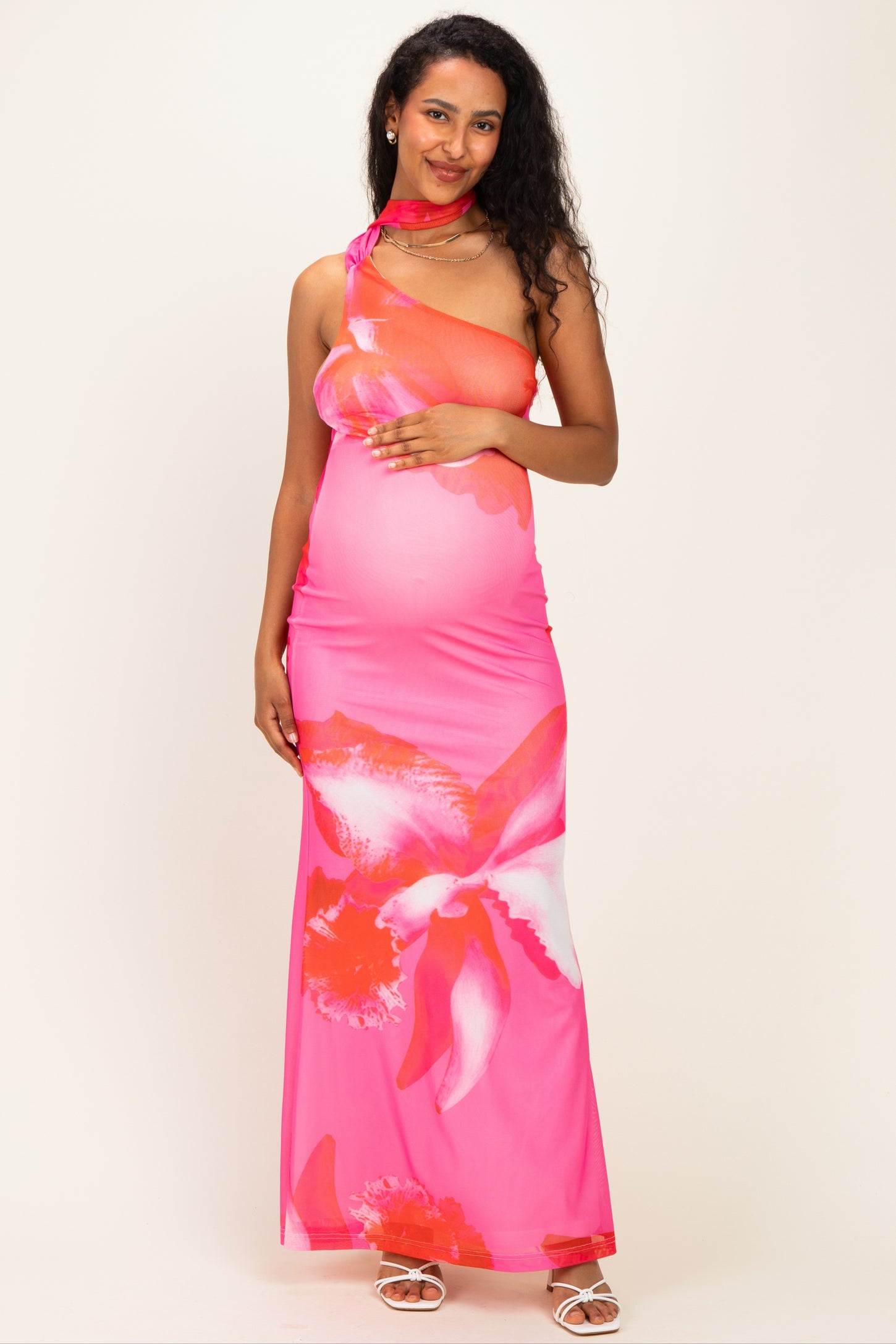 woman wearing a pink floral maternity maxi dress and holding her baby bump with one shoulder strap