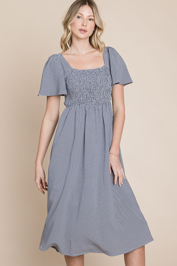 woman wearing a blue and white gingham midi dress with short puff sleeves and a smocked bodice