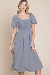 woman wearing a blue and white gingham midi dress with short puff sleeves and a smocked bodice