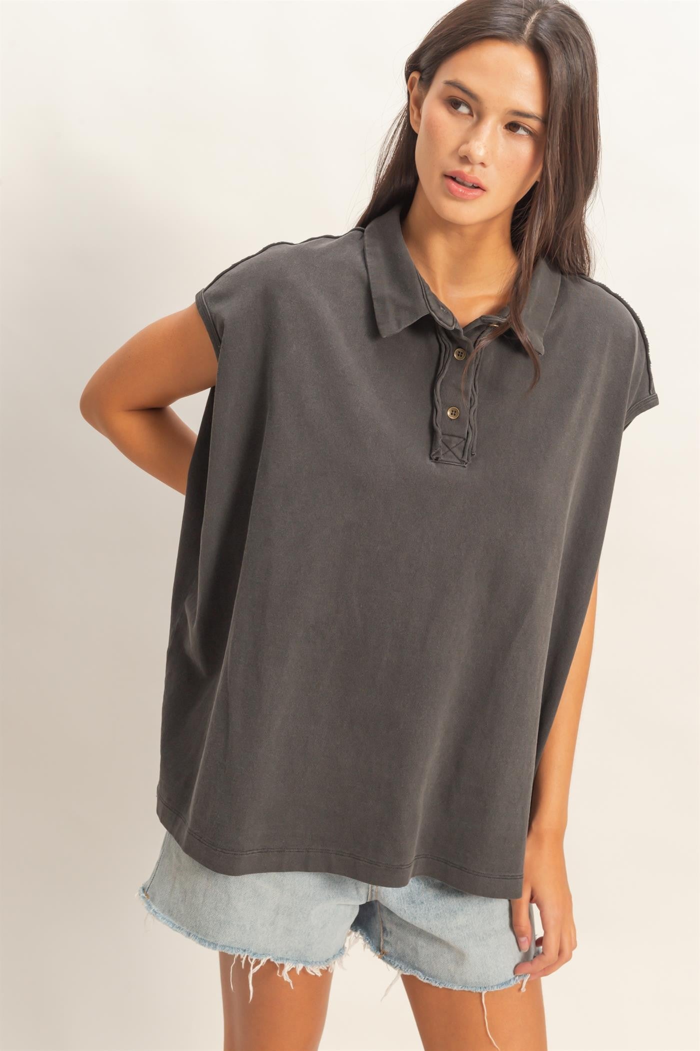 woman wearing a dark gray oversized polo shirt with a button placket and paired with distressed denim shorts
