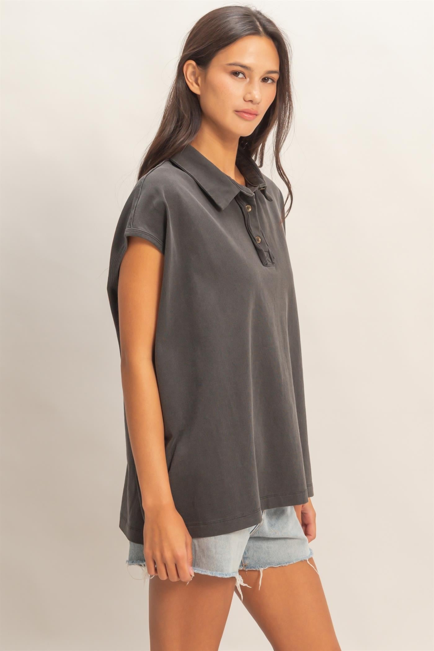 woman wearing a dark gray short sleeve polo shirt with buttons and light blue distressed shorts