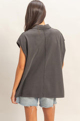 woman wearing a dark gray oversized sleeveless top with a collar, paired with denim shorts