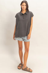 woman wearing a dark gray oversized polo shirt with short sleeves and distressed denim shorts, paired with brown sandals
