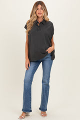 woman wearing a charcoal gray maternity top and blue flared jeans, standing with one hand in her pocket