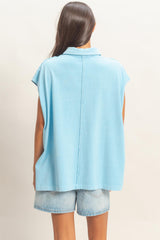 woman wearing a light blue oversized sleeveless top paired with denim shorts, viewed from the back