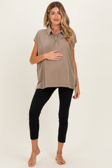 woman wearing a taupe maternity polo shirt and black leggings, holding her baby bump