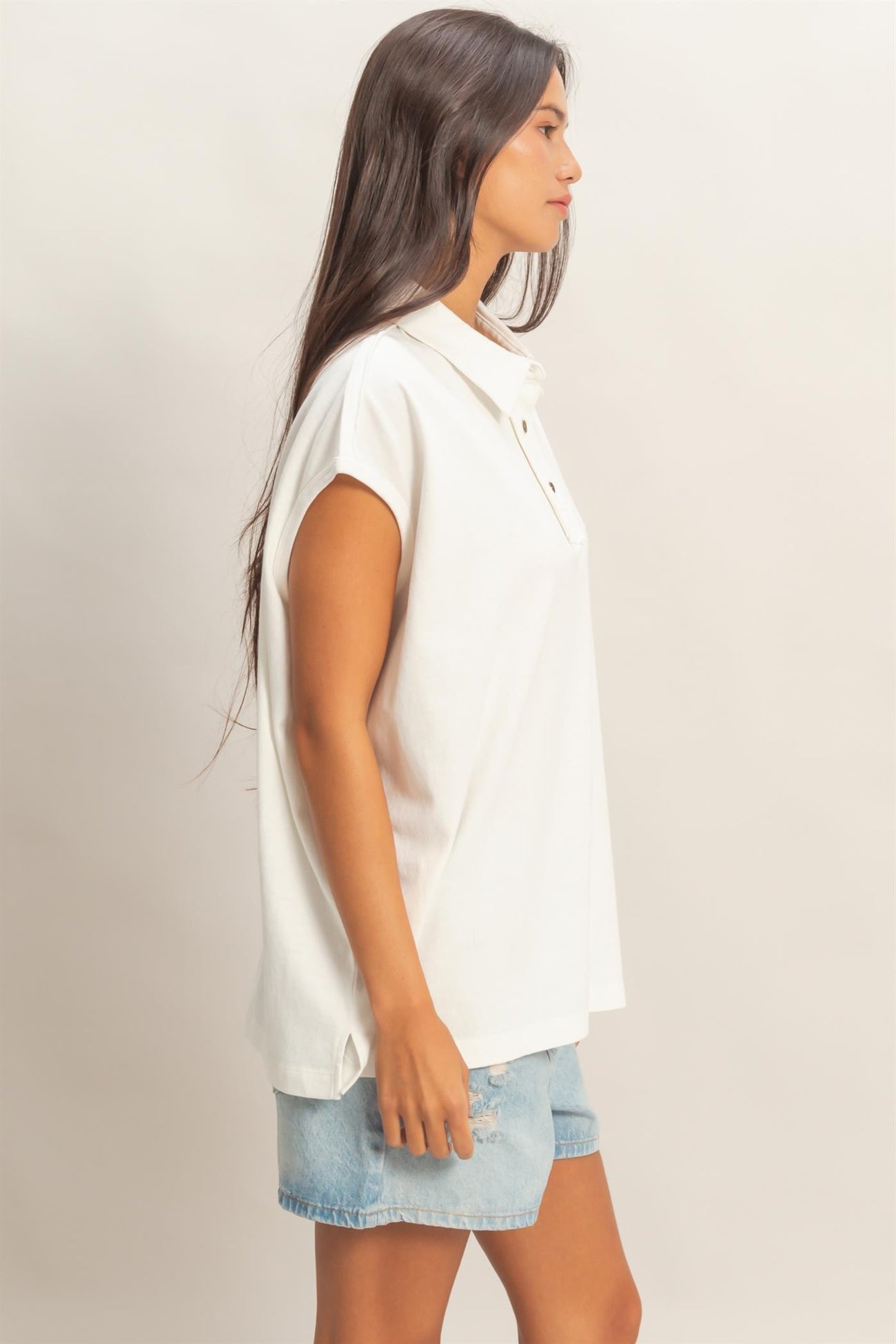 woman wearing a white short sleeve polo shirt and denim shorts, standing sideways with long hair down