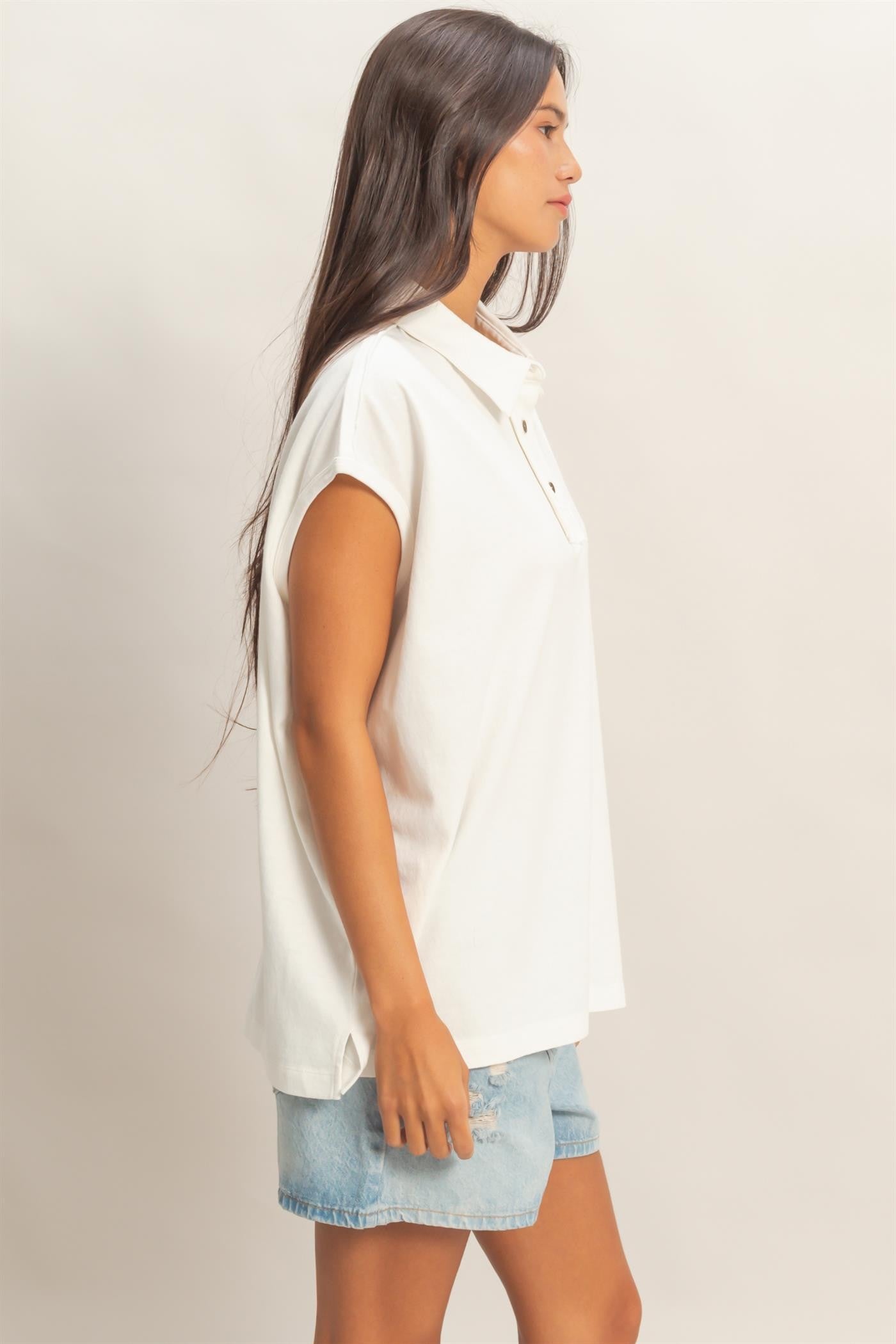 woman wearing a white short sleeve polo shirt and denim shorts, standing sideways with long hair down