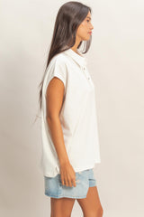 woman wearing a white short sleeve polo shirt and denim shorts, standing sideways with long hair down