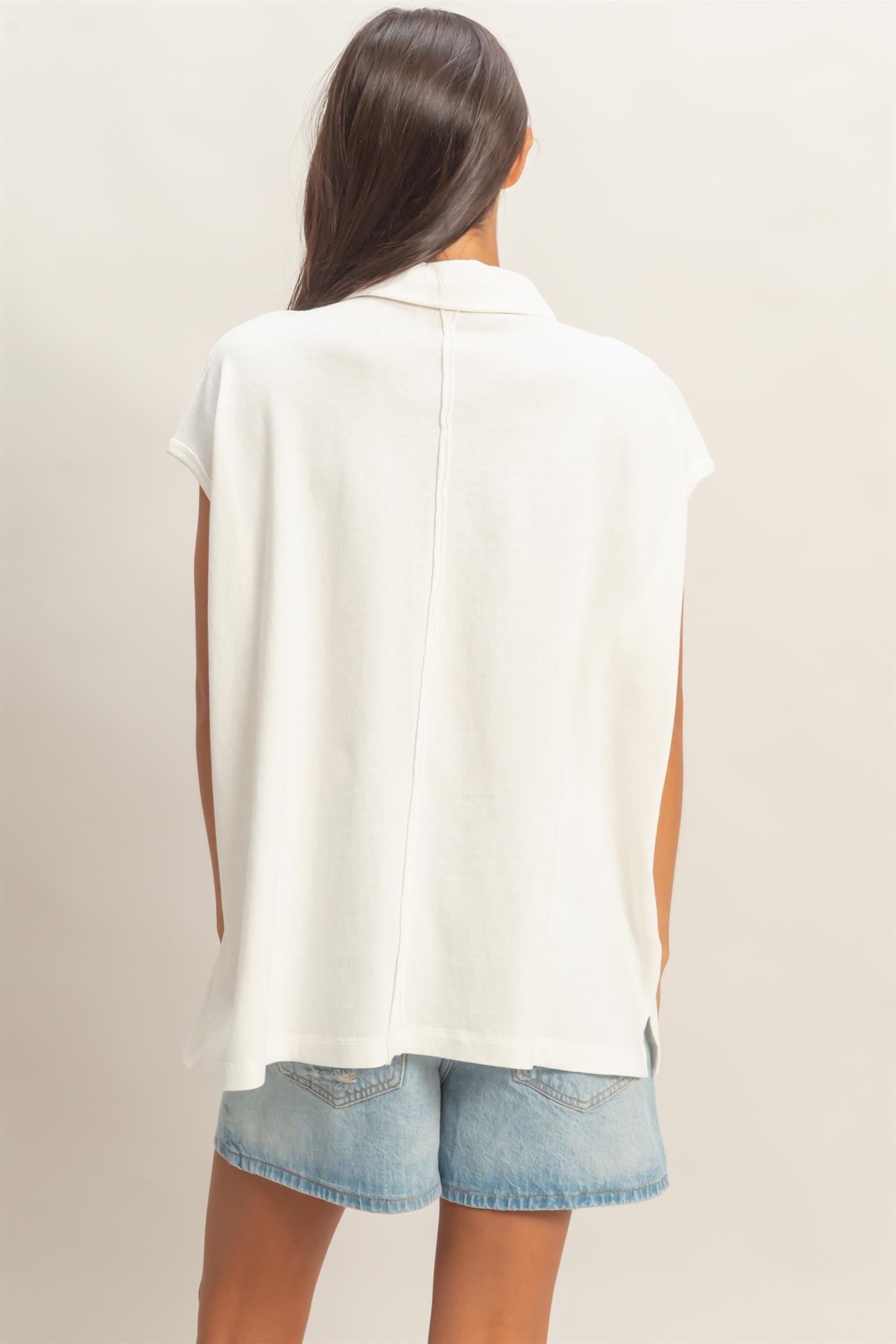woman wearing a white short sleeve oversized top with a back seam, paired with denim shorts