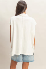 woman wearing a white short sleeve oversized top with a back seam, paired with denim shorts